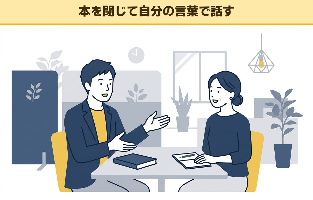 会議テーブルで閉じた本を前に、身ぶりを交えて同僚に要点を説明する男性と、うなずいて聞く女性